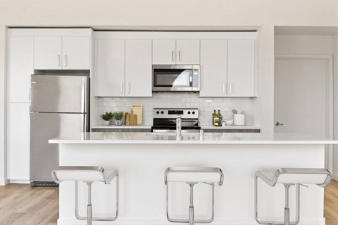 A modern kitchen with white cabinets and a white island with three stools.