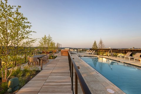 A wooden walkway leads to a pool with a table and chairs on the side.