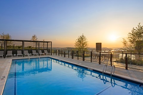 A swimming pool with lounge chairs and a sunset in the background.