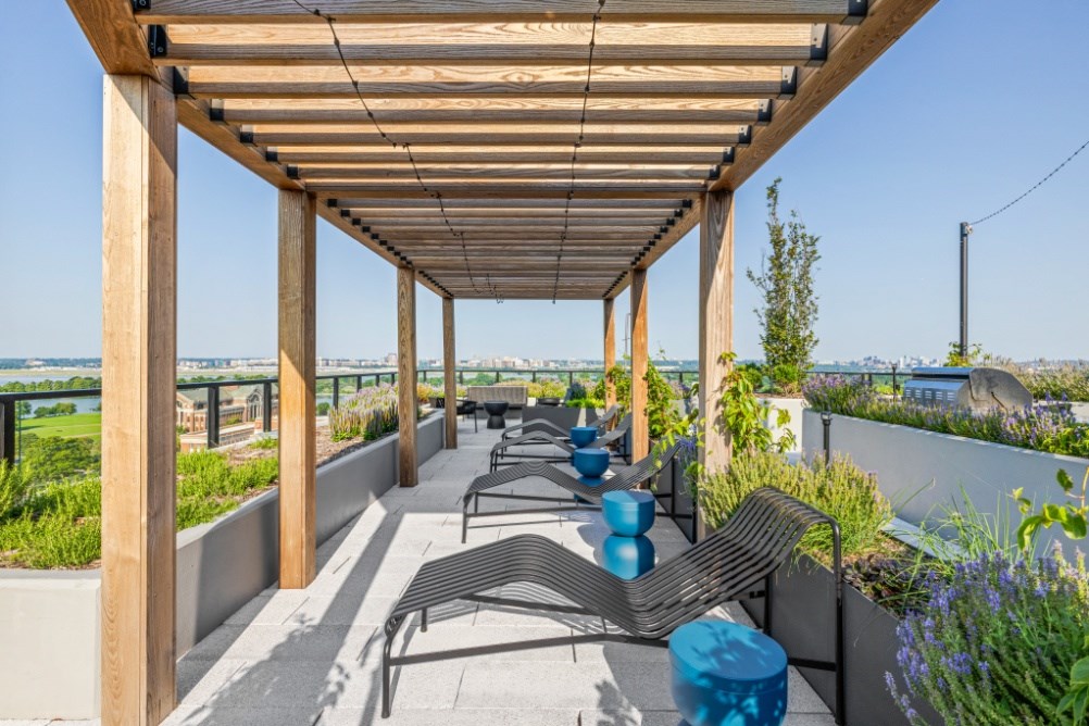 A wooden pergola with benches and tables is situated on a rooftop with a view of the water.