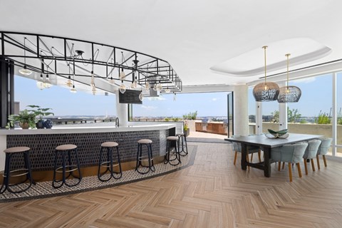 A modern bar area with a wooden floor and a large window overlooking the city.