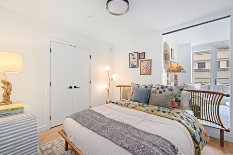 A bedroom with a bed, nightstand, and a window overlooking a cityscape.