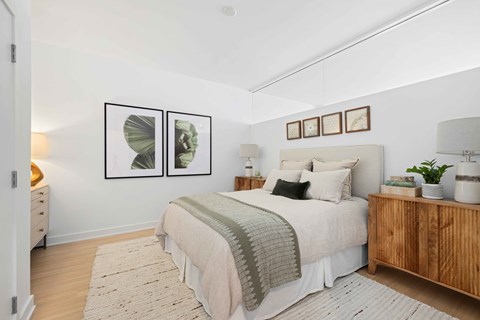 A bedroom with a bed, nightstand, and two framed pictures on the wall.