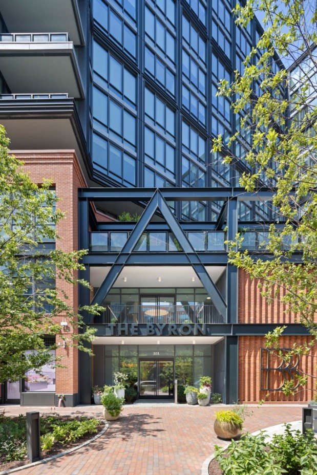 The entrance to a building with a glass facade and a brick walkway.