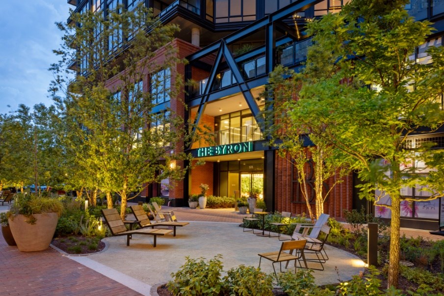 A modern building with a glass entrance and a courtyard with chairs and trees.