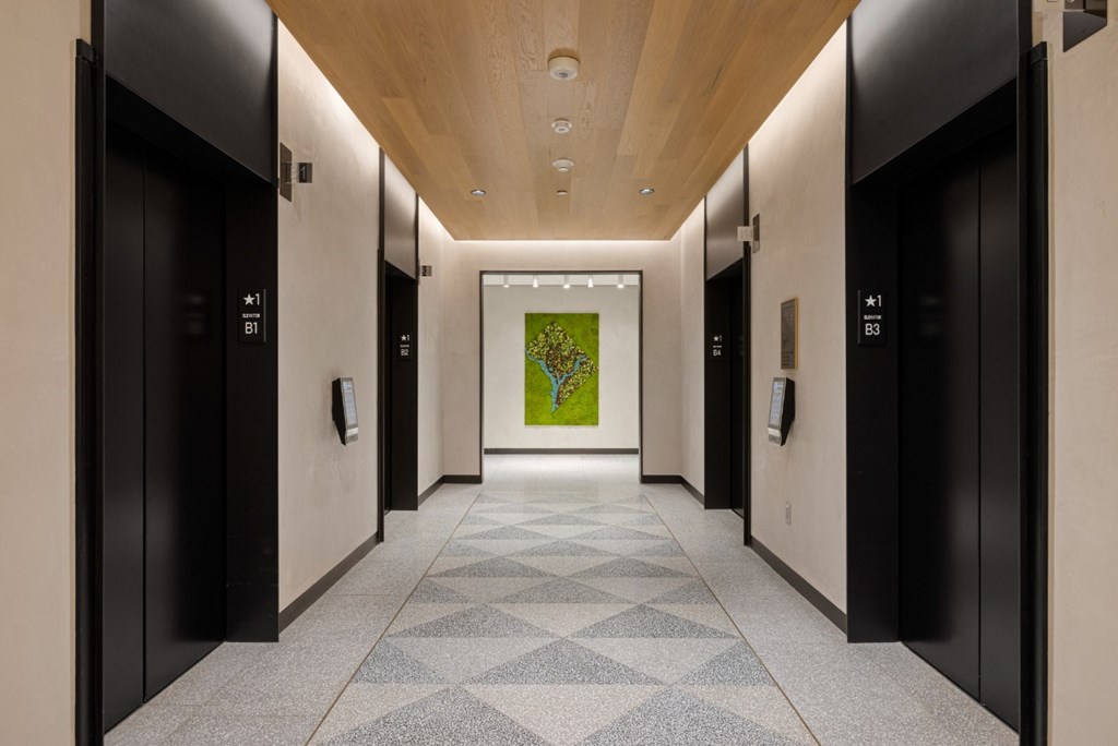 A long hallway with a green painting in the middle and elevators on both sides.