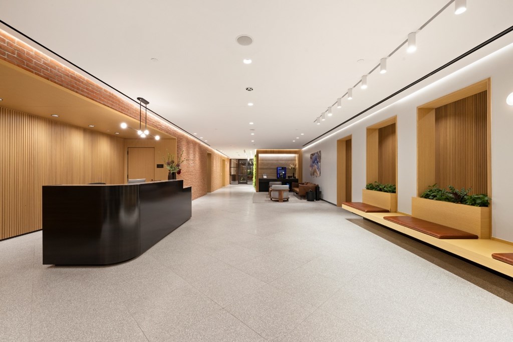 A long hallway with a black reception desk on the left and wooden planters on the right.