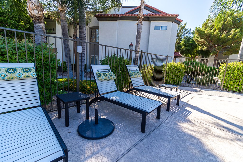 two lounge chairs and a coffee table sit on a concrete patio in front of a white building