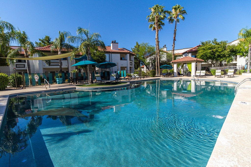 a large swimming pool with umbrellas and buildings in the background