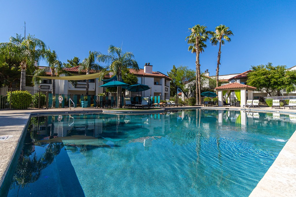 a large pool with umbrellas and palm trees in the background