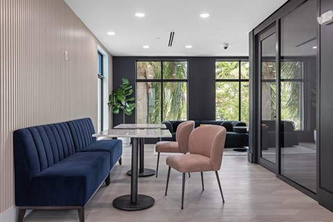 A blue sofa sits next to a table with a pink chair in front of a glass door.