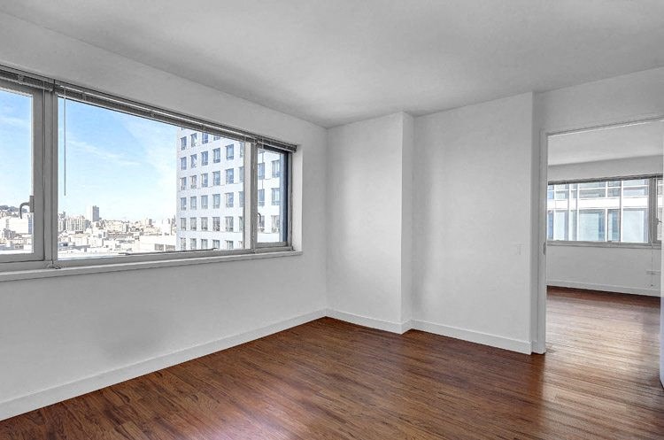an empty bedroom with a large window and hardwood floors