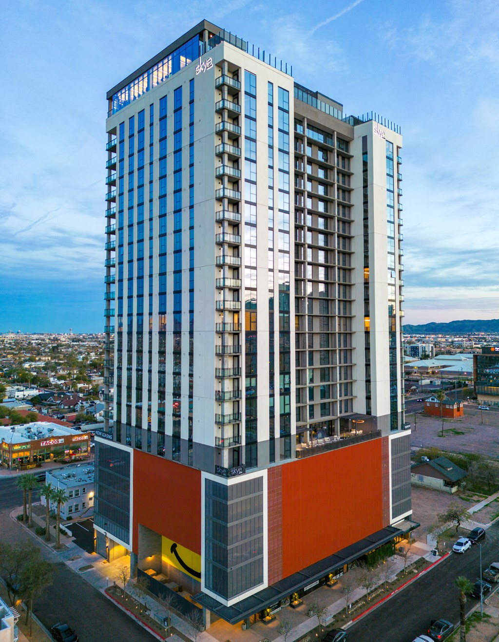 a tall building with a red and white facade and a city in the background