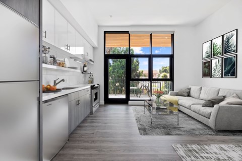 A modern kitchen with a refrigerator on the left and a living room with a couch and a coffee table on the right.