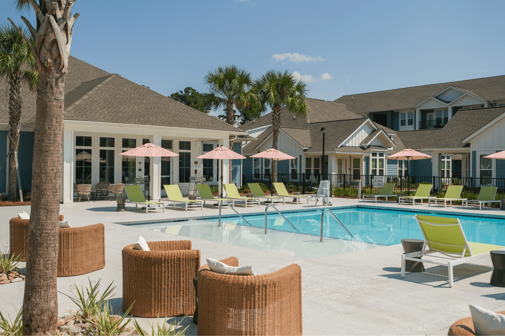 A pool area with chairs and umbrellas in front of a building.