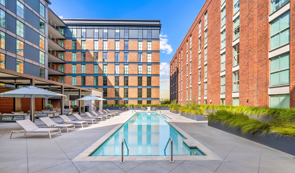 A swimming pool surrounded by lounge chairs and umbrellas in front of a modern building.