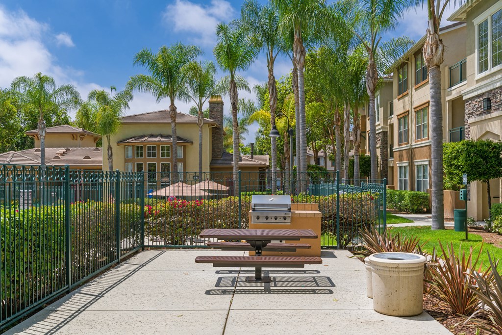 A park area with a picnic table and benches in front of a gated community.