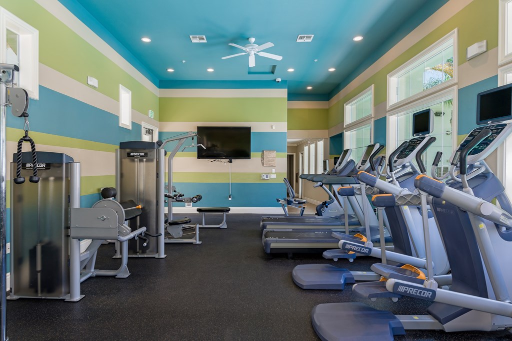 A gym with a row of treadmilers and a television.
