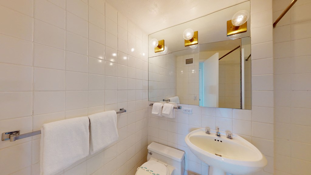 a bathroom with white tiles and a white sink with a mirror above it