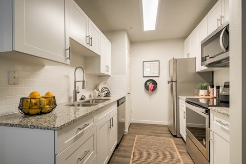 A kitchen with white cabinets and a bowl of oranges on the counter.