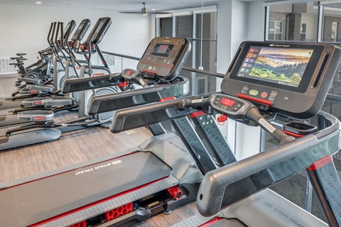 A row of treadmills in a gym with a screen on the front.