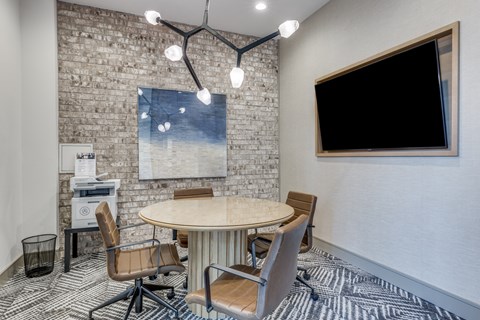 A conference room with a round table and chairs, a brick wall, and a blank TV screen.