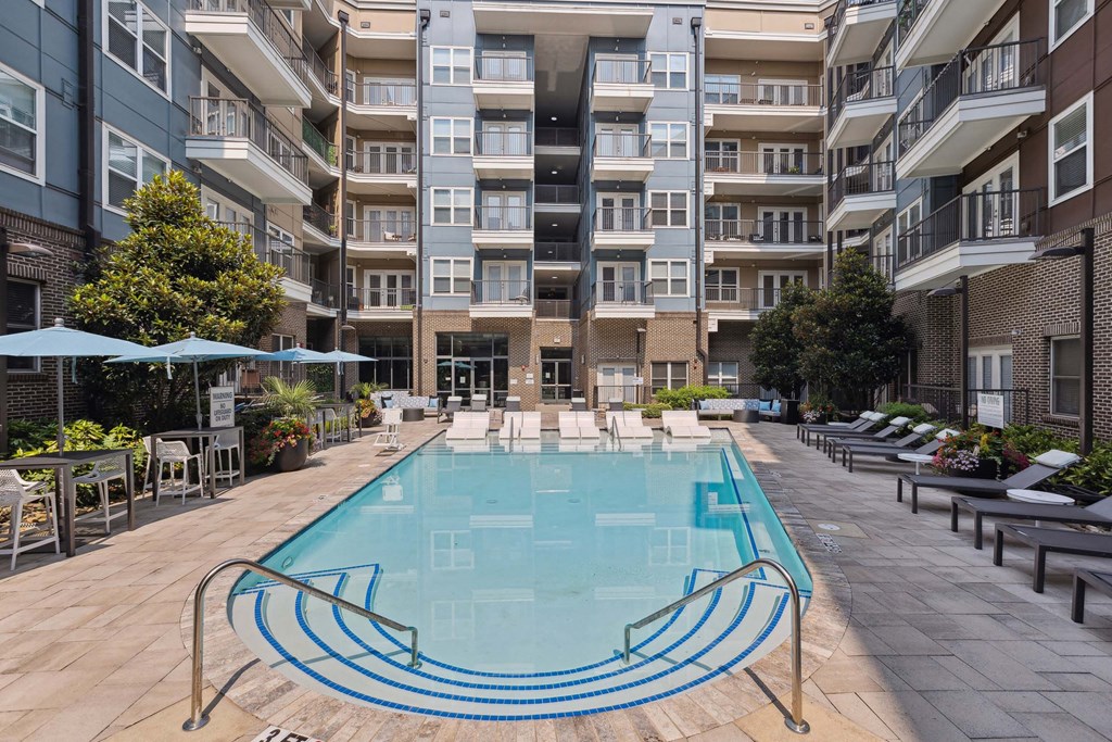 an outdoor swimming pool with lounge chairs and umbrellas in front of an apartment building