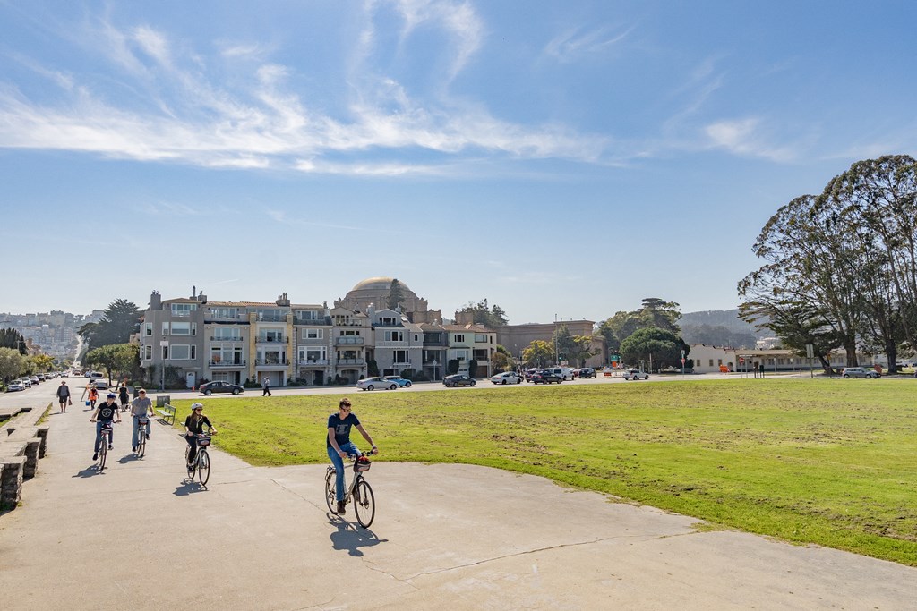 a group of people riding bikes on a sidewalk next to a grassy field