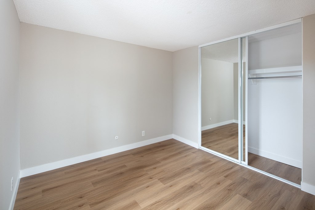 a bedroom with hardwood floors and a mirrored closet