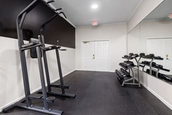 A gym with a weight bench, dumbbells and a mirror.