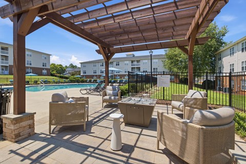 A patio with a pool and chairs under a wooden pergola.