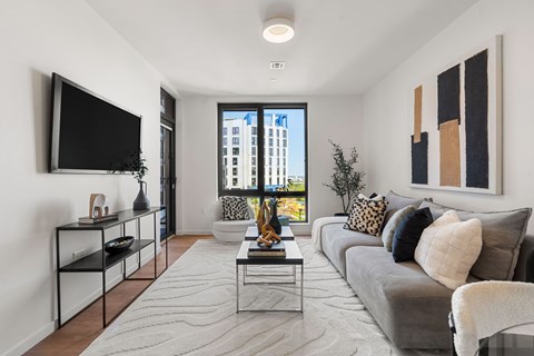 A modern living room with a grey couch and a flat screen TV mounted on the wall.