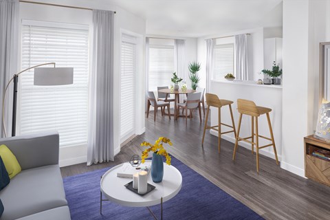 A modern living room with a grey sofa, a coffee table, and a dining table set up.