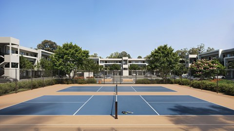A tennis court is surrounded by buildings and trees.