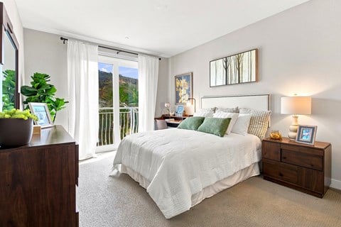A bedroom with a large bed, a nightstand, and a window with a view of the outdoors.