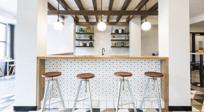 a bar with three stools in front of a white tiled counter with wood