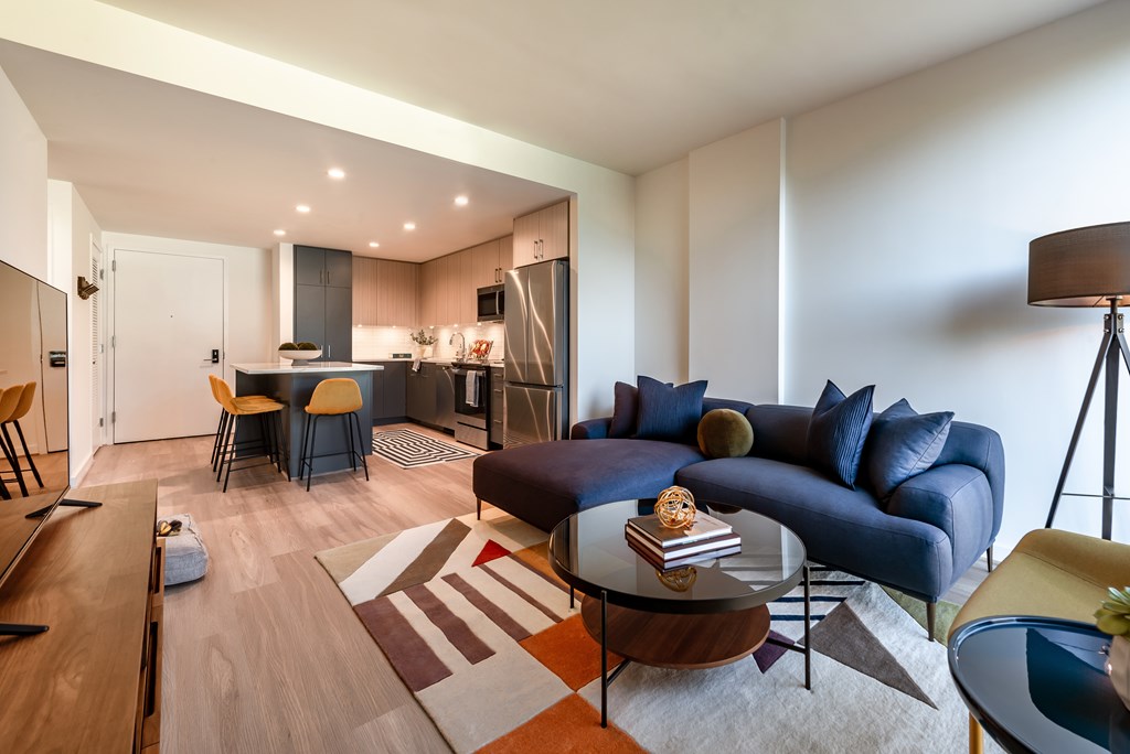 A modern living room with a kitchen in the background.