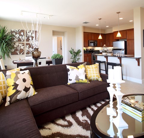 a living room and kitchen with a brown couch and yellow pillows