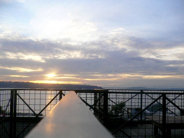 a view of the sunset over the water from the top of a bridge