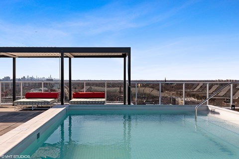 A swimming pool with red chairs and a wooden pergola.