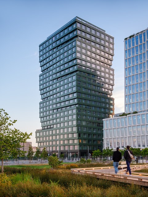 Two men walking on a wooden platform in front of a tall glass building.