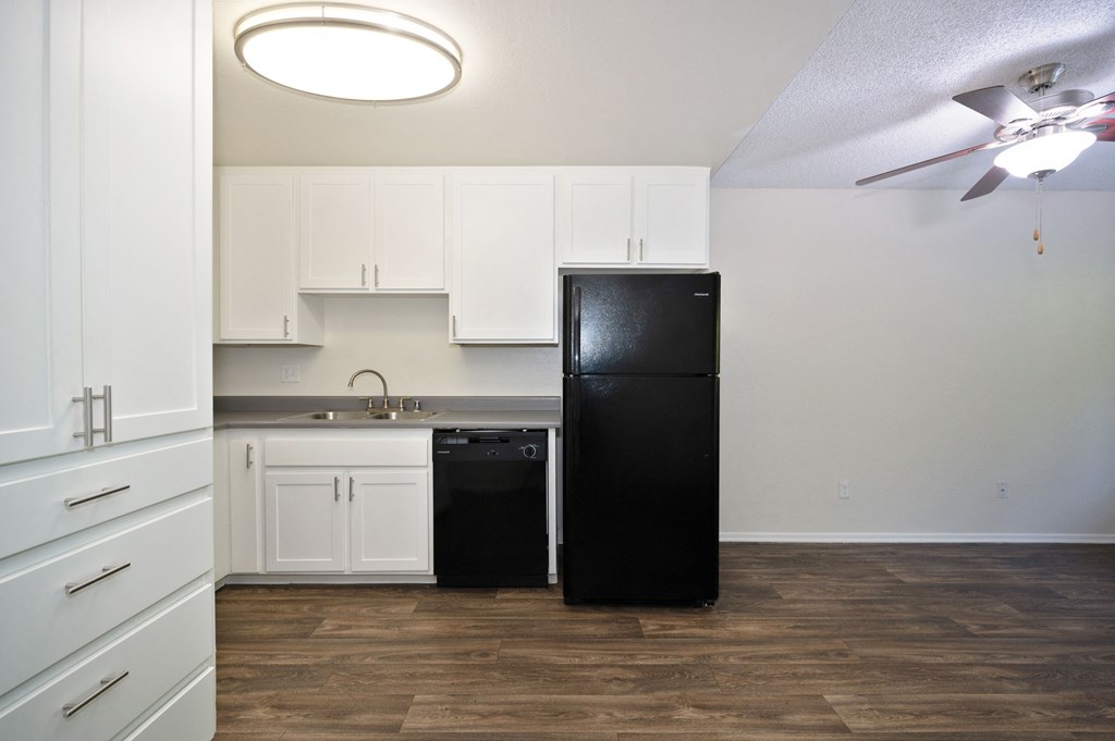 a studio apartment kitchen with white cabinets and a black refrigerator