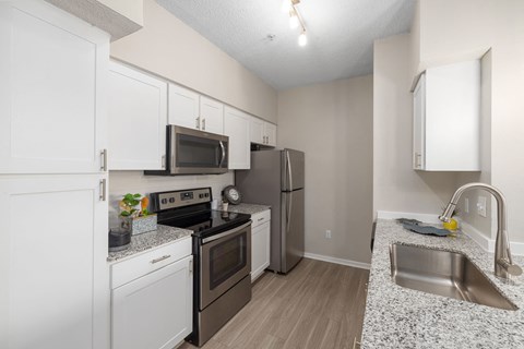 A kitchen with a black stove top oven, black microwave, black refrigerator, and a white sink.