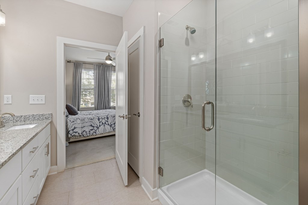 A bathroom with a walk-in shower and a bedroom with a window.