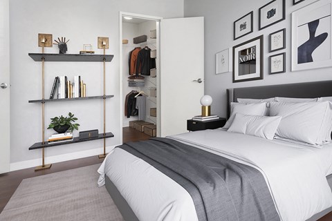 A bedroom with a bed, a shelf with books and a plant, and a wall with framed pictures.