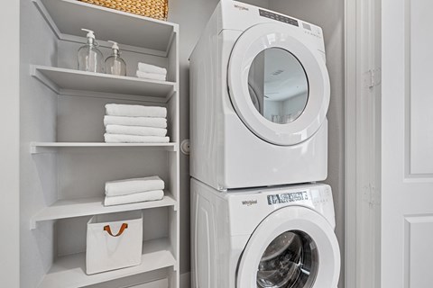 A white washing machine is stacked on top of a white dryer in a laundry room.
