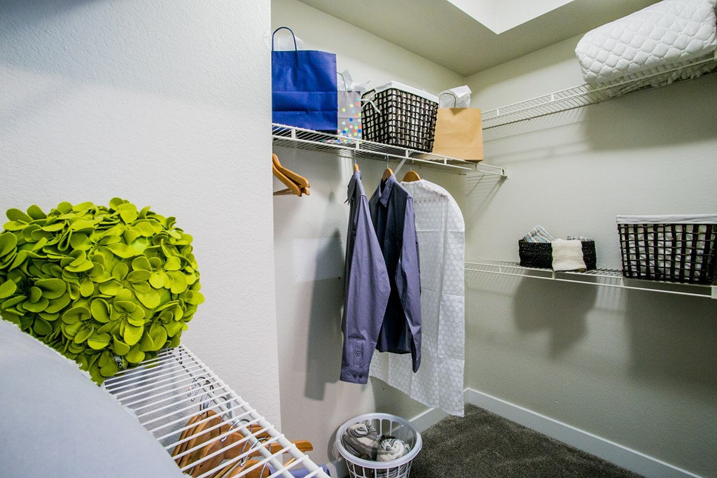 A closet with clothes hanging and baskets on the shelves.