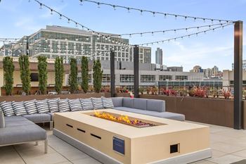 A modern outdoor seating area with a fire pit and string lights.