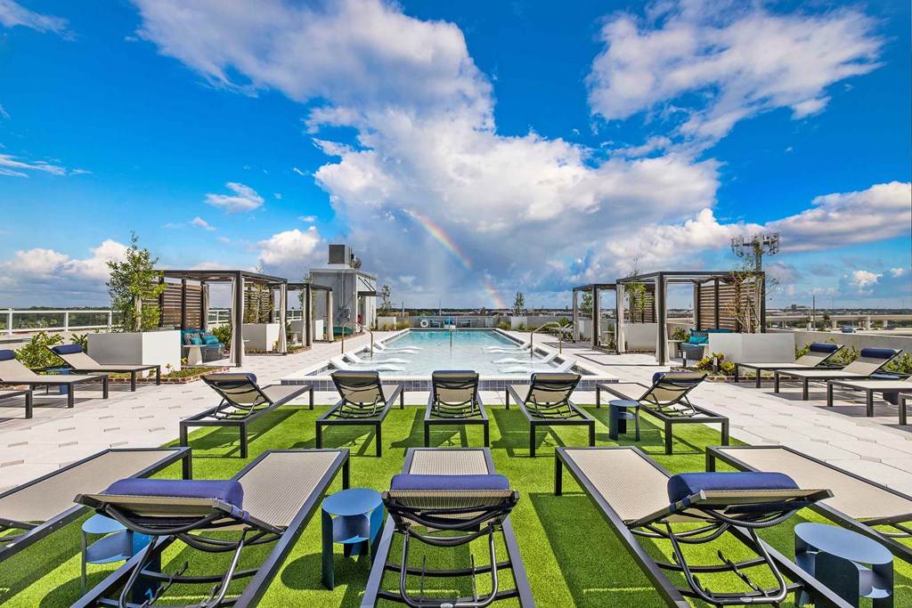 a rooftop pool with lounge chairs and tables and a rainbow in the sky