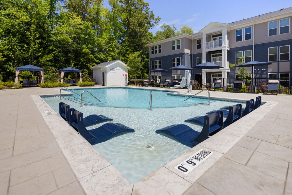A swimming pool surrounded by lounge chairs and umbrellas in front of a residential building.